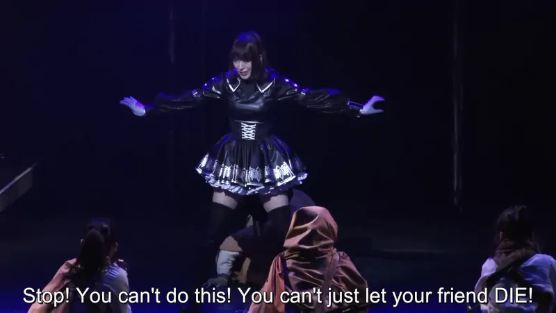 A subtitled still from the 1.2 version of the YoRHa play. No. 21 intervenes to stop a summary execution, saying 'Stop! You can't do this! You can't just let your friend die!'