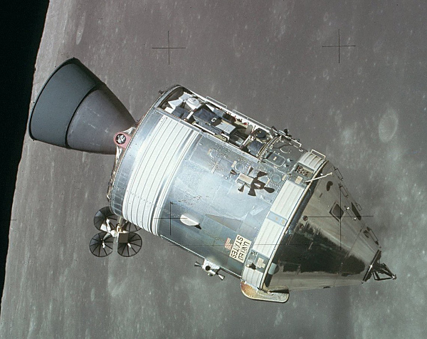 A photograph of the Apollo Command and Service module, a shiny metal cylinder with a conical nose, various instruments on the side including antennae and reaction control thrusters, and a long nozzle on the back.