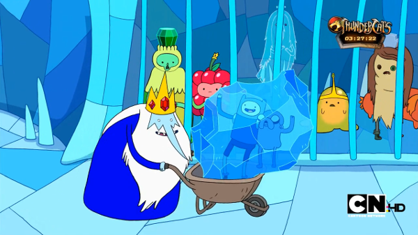 The Ice King wheels Finn and Jake, who are frozen in a block of ice, past a cell full of princesses in various shapes.