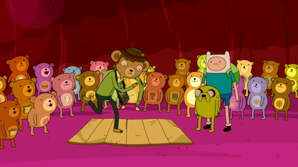 Party Pat, a bear in a green cardigan and a trilby, breakdances on a sheet of cardboard in front of an audience of much smaller bears.