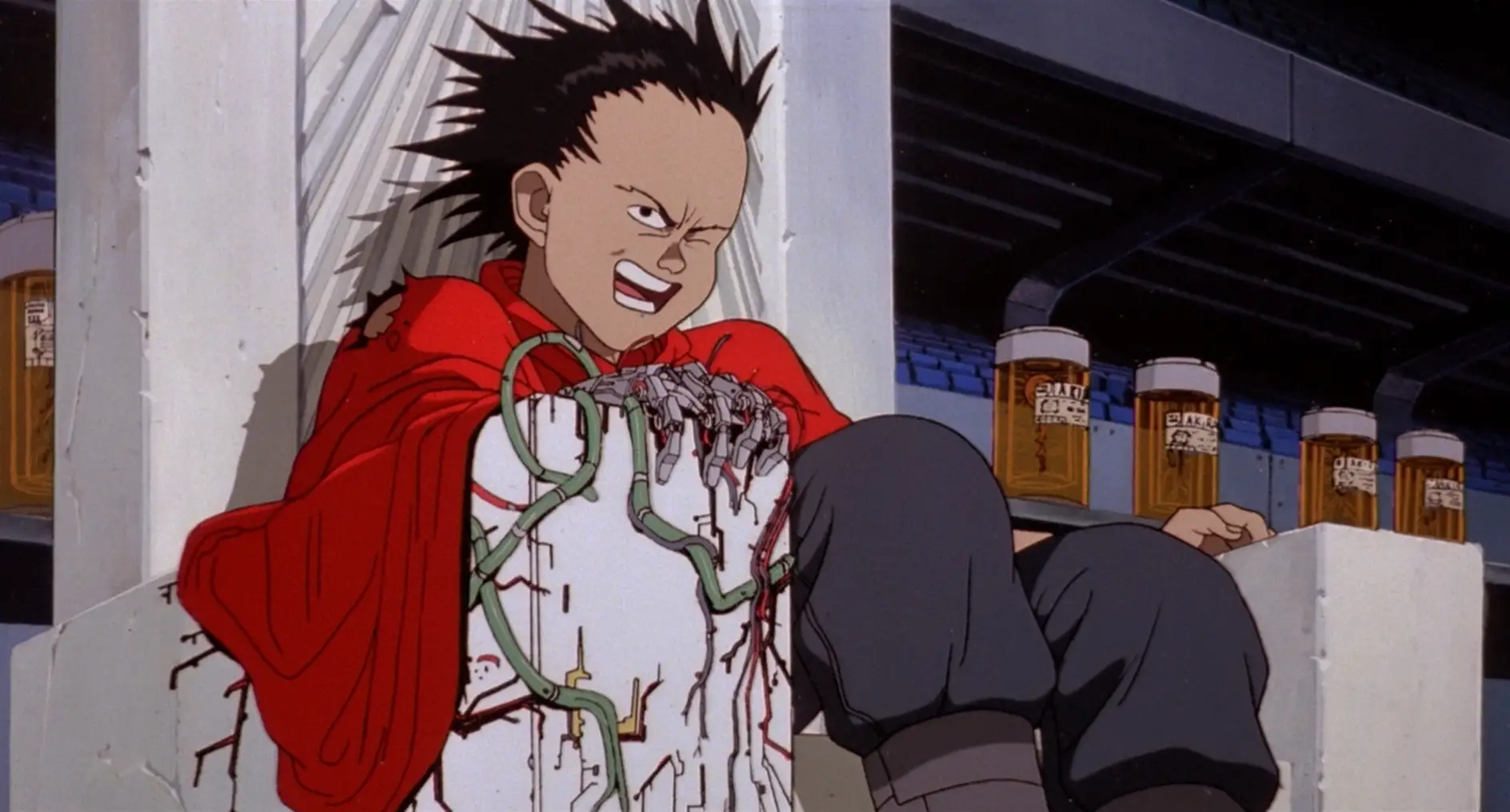 Still from Akira. Tetsuo sits on a throne in a red cape, with a leering expression. Green wires grow out of his robot arm. Behind him, a row of bottles contains tissues from Akira himself.