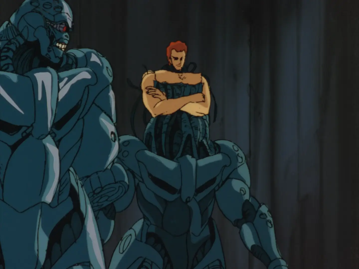 Still from Bubblegum Crisis (1987) showing two Boomers. One is just a metallic robot with a metal skull, but the other has a human shoulders connected to the bulky metal frame by a mass of tentacles.
