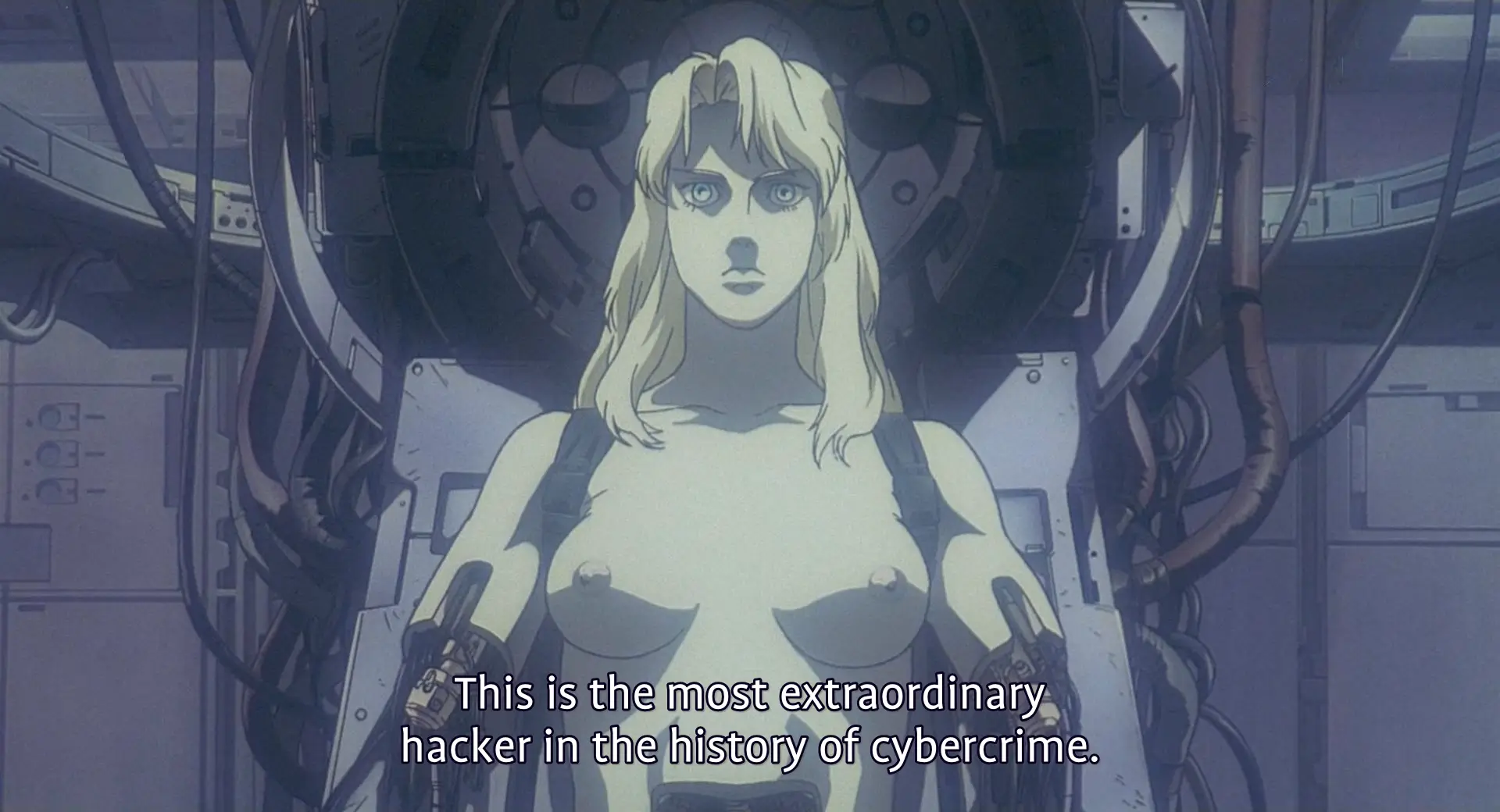 Still from GitS. The Puppet Master's constructed body is placed naked in an experiment rig with arms and lower torso removed. Her expression is neutral. A goverment minister is saying 'This is the most extraordinary hacker in the history of cybercrime'.