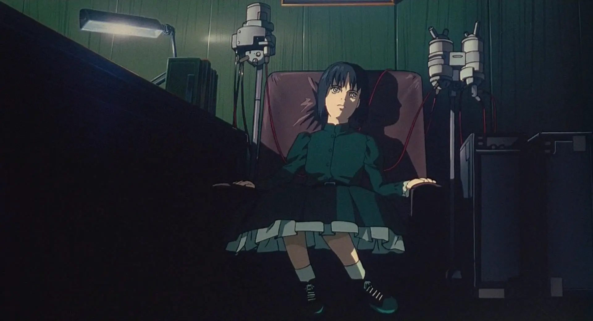 A still from GitS. The gestalt of the Major and the Puppet Master now inhabits a doll-like body wearing a green dress, sitting in a chair connected to various drip-like devices.
