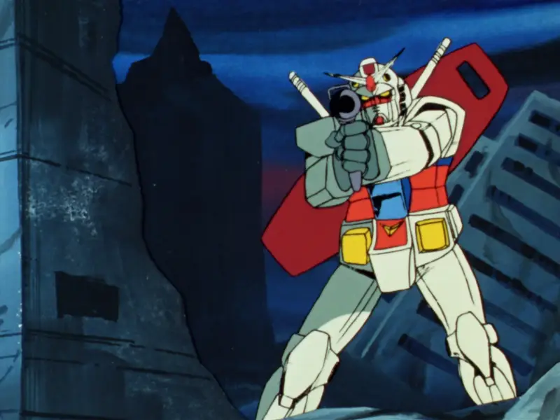 Still from Mobile Suit Gundam showing a Gundam aiming its gun at the camera. It is a blocky robot with a bright white surface with red, yellow and blue accents. The helmet is ornamented like a samurai helmet.