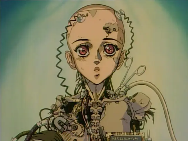 Still from Gunnm (1993). Gally is in the process of repairs, a mechanical body that ends somewhere in the ribcage. Various cables are attached to her with electrodes. She stares at the camera with an innocent expression.