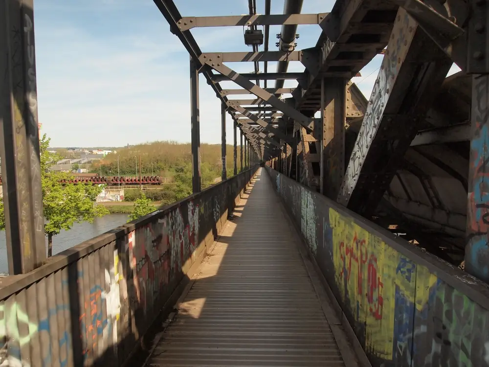 A view down the pedestrian part of a long rail bridge, stretching away in a very straight line.